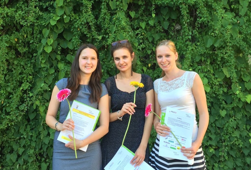 3 Personen stehen nebeneinander mit Blumen und Urkunden in den Händen