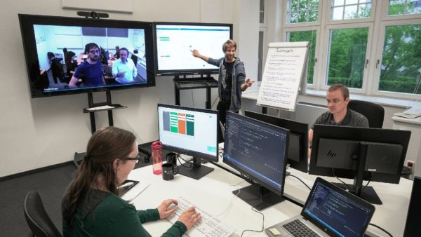 Ein Team arbeitet verteilt über zwei Standorte zusammen und ist per Videokonferenz zusammengeschaltet.