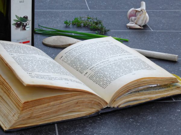 Altes Buch mit Rezepten liegt neben Koch- und Küchenutensilien