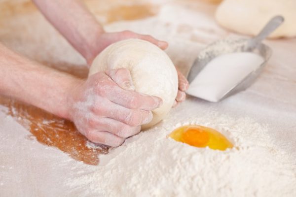 Hands kneading a dough, baking ingredients and utensils lying on the side