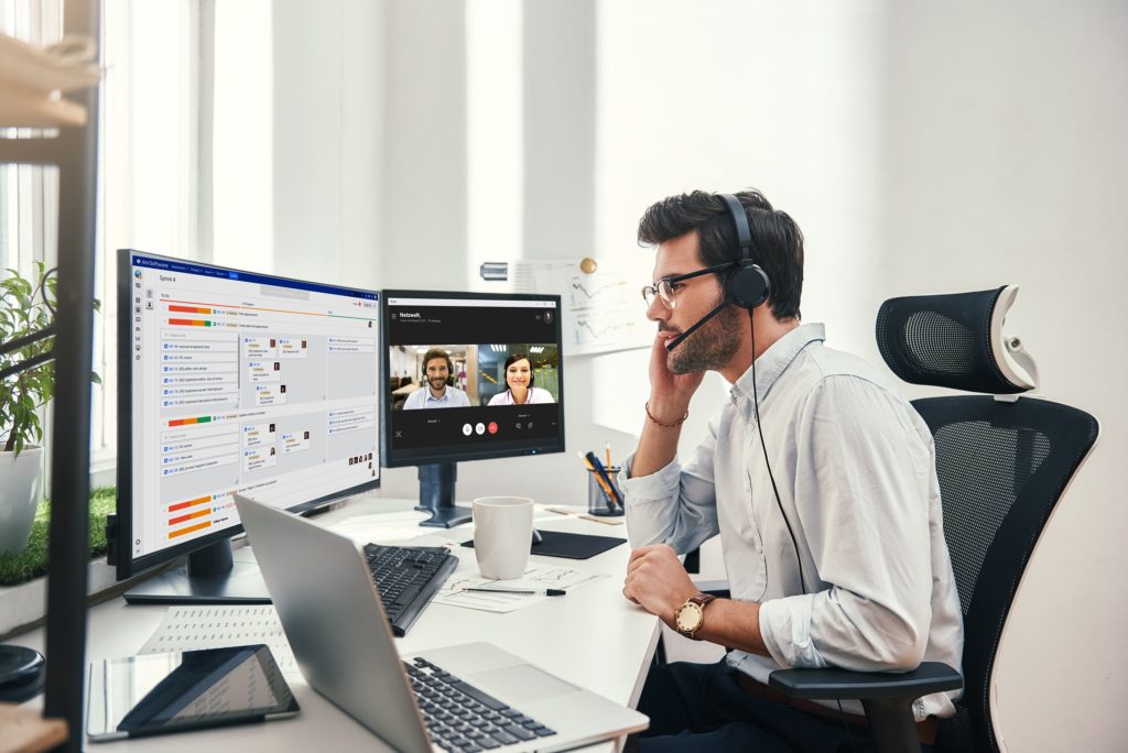 Person sits in front of a laptop and severals screens during a video conference using the ETEOboard tool for distributed collaboration