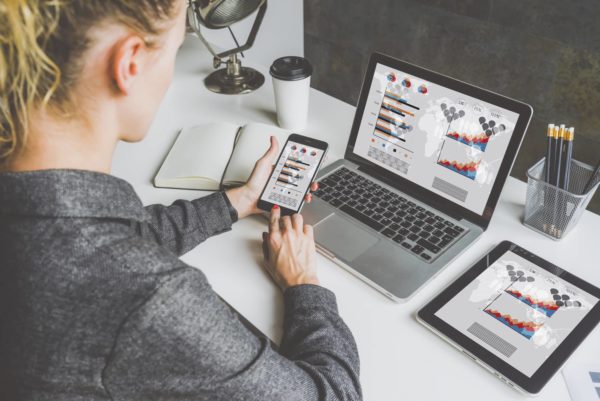 Symbolic picture: A woman is sitting at a desk with a laptop, tablet and smartphone. The user interfaces show the same dashboards.